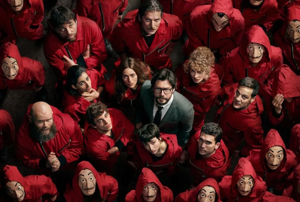 Money Heist Review - The Professor and the gang standing together in red jumpsuits.