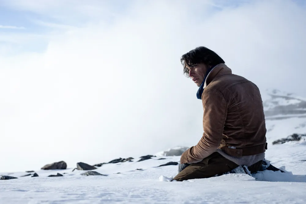 Enzo Vogrincic as Numa Turcatti sitting alone in the snow next to the plane wreckage.