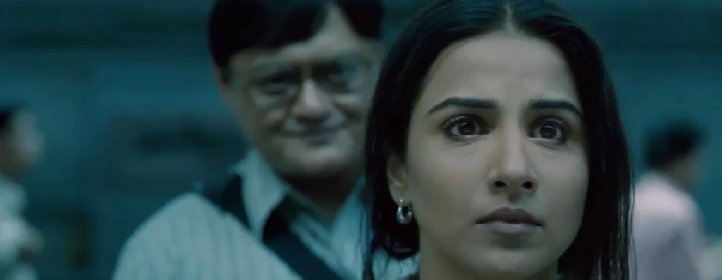 Bob Biswas standing behind Vidya Bagchi at the Kolkata metro station.