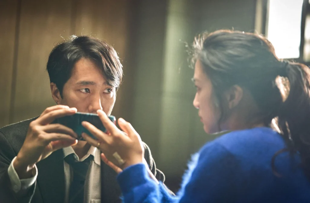 Detective Jang and Song looking at each other while holding a phone in Decision To Leave.